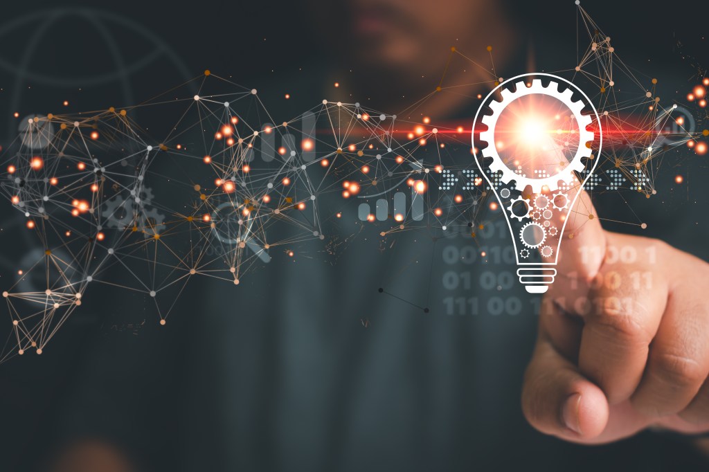 Glühbirne mit Zahnrad, zu der Informationen und Ideen laufen. Die Glühbirne wird von einem Mann angetippt.